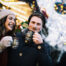„Ein lachendes Paar trinkt heißen Punsch auf einem festlich beleuchteten Weihnachtsmarkt.“